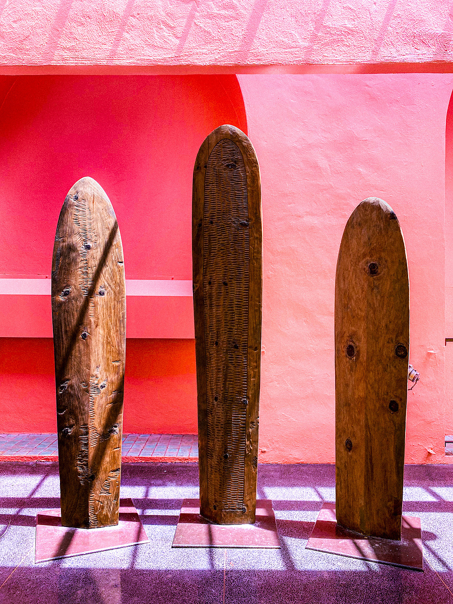 Three old wooden surfboards standing against a pink and red wall