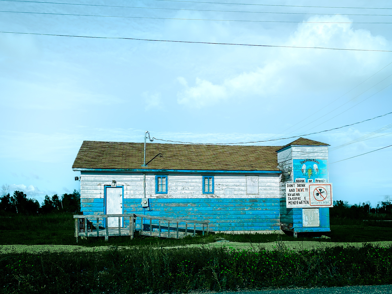 Weathered blue and white wooden building under power lines and a blue sky
